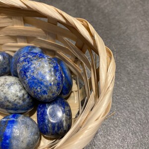 May include: A collection of smooth, polished, blue and white lapis lazuli stones in a woven basket.
