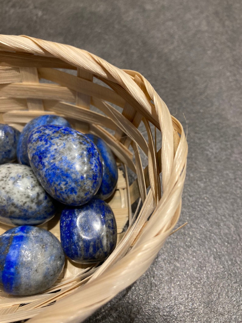 May include: A collection of smooth, polished, blue and white lapis lazuli stones in a woven basket.