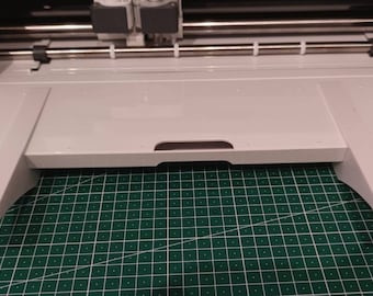 Könnte beinhalten: Eine weiße Schneidemaschine mit einer weißen Plattform, die sich nach vorne erstreckt. Die Plattform hat auf jeder Seite zwei weiße Beine.