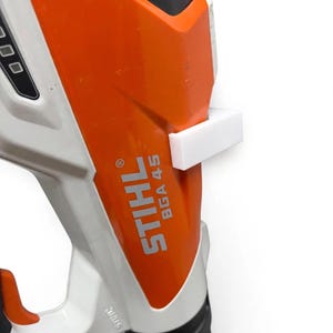 Peut inclure: Un souffleur de feuilles Stihl BGA 45 doté d'un boîtier en plastique blanc et orange avec une fixation rectangulaire blanche montée sur le côté. La marque et le numéro de modèle sont imprimés en blanc sur la section orange de l'outil.