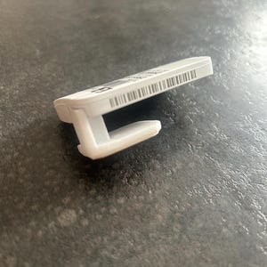 Op de afbeelding: Witte plastic haak met een barcode-etiket op de achterkant. De haak is ontworpen om items aan een muur of ander oppervlak te hangen.