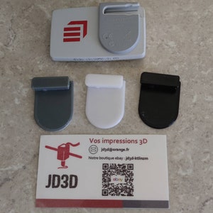 Op de afbeelding: Een witte kaart met de tekst "JD3D" en een QR-code. De kaart bevat ook de tekst "Vos impressions 3D" en een e-mailadres. Er zijn drie 3D-geprinte haken op de afbeelding: een grijze, een witte en een zwarte.