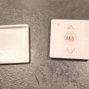 Pode incluir: Dois componentes quadrados de plástico branco. Uma peça é uma moldura oca com uma borda elevada. A outra peça apresenta uma superfície de grade texturizada com uma seta para cima, uma seta para baixo e a palavra "my" no centro.