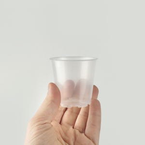 Peut inclure: Un pot en plastique transparent avec des trous de drainage au fond. Le pot est tenu dans une main.