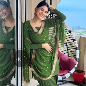 May include: A woman wearing a green salwar kameez with gold polka dots and a gold trim. She is wearing a matching dupatta with a gold border. The outfit is a traditional Indian garment.