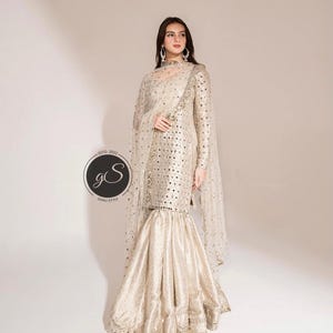 May include: A formal, gold-colored ensemble featuring a long-sleeved top with mirror embellishments and a flared skirt. The outfit includes a sheer, dotted shawl and is suitable for special occasions. The logo "GS GARU STYLE" is visible.