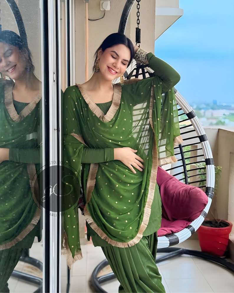 May include: A woman wearing a green salwar kameez with gold polka dots and a gold trim. She is wearing a matching dupatta with a gold border. The outfit is a traditional Indian garment.