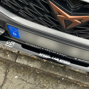 Könnte beinhalten: Ein schwarzes und silbernes Auto mit einer schwarzen Frontstoßstange und einem schwarz-weißen Aufkleber mit der Aufschrift "SPEED. I AM SPEED". Das Auto hat einen schwarzen Kühlergrill mit einem kupferfarbenen Logo. Das Auto hat ein Nummernschild mit der Aufschrift "AUTOHAUS R. KÖHLER SIEGEN".