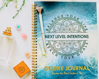 May include: A blue and green journal with a gold spiral binding. The cover features a mandala design with the text "Balance Your Life, Next Level Intentions, Reach Your Goals" and "Deluxe Journal, Become the Best Version of You".