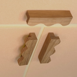 Könnte beinhalten: Drei Holzstücke mit einer wellenförmigen Kante. Die Stücke sind hellbraun und haben eine natürliche Holzoptik. Die Stücke sind in Dreiecksform angeordnet.