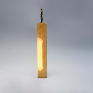 May include: A wooden wall mount with a rectangular cutout, featuring a light brown finish and a screw at the top.