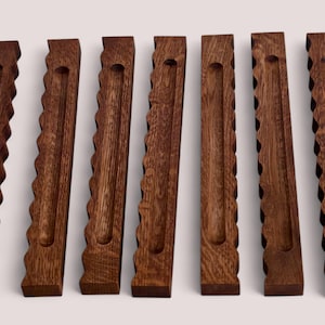 May include: Seven wooden, rectangular pieces with a dark brown finish. Each piece has a unique, decorative edge, with variations including scalloped and zigzag patterns. A small, circular indentation is present on each piece.