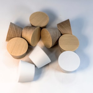 May include: A collection of ten conical objects, including several light-colored wooden pieces with visible grain patterns and three solid white pieces. Each item features a flat circular top and a tapered base, arranged in a cluster.