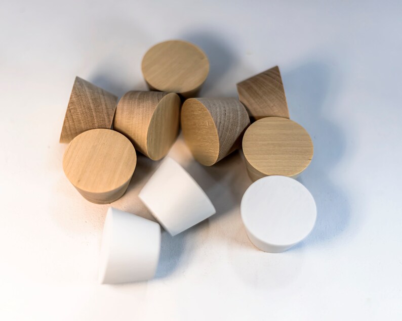 May include: A collection of ten conical objects, including several light-colored wooden pieces with visible grain patterns and three solid white pieces. Each item features a flat circular top and a tapered base, arranged in a cluster.