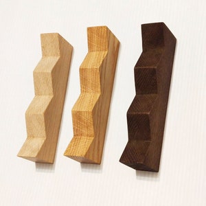 May include: Three wooden wall-mounted shelves in the shape of a staircase. The shelves are made of different types of wood, one is light brown, one is a medium brown, and one is a dark brown.