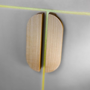 May include: Two light-toned wooden cabinet pulls with a semi-circular profile, positioned vertically side-by-side. The natural wood grain is visible on the flat surfaces, and a thin, bright neon yellow line runs horizontally and vertically between them.