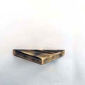 Może przedstawiać: Trójkątna drewniana półka z wykończeniem w kolorze czarnym i brązowym. Półka jest zamontowana na białej ścianie.