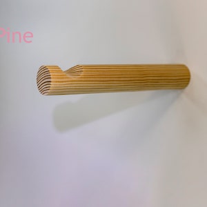 Peut inclure: Un crochet mural en bois de pin. Le crochet est en forme de petit cylindre arrondi avec un crochet incurvé à l'extrémité. Le crochet est monté sur un mur blanc.