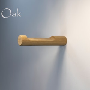 May include: A wooden wall-mounted towel rack made of oak wood. The rack has a rounded end and a cutout in the middle for hanging towels.