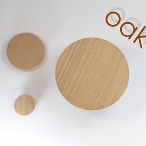 May include: Three round wooden coasters made of oak wood. The largest coaster is in the centre of the image, with two smaller coasters to the left and below it.