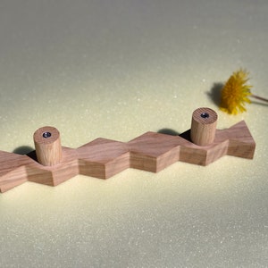 May include: A wooden wall hook with two rounded knobs. The hook is shaped like a zig-zag line and is made of light brown wood.