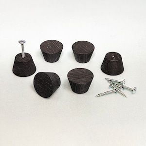 May include: A set of six dark brown, tapered wooden knobs with a visible wood grain texture. Each knob has a flat circular top and a wider base. One knob is attached to a metal screw, and four additional metal screws are included separately.