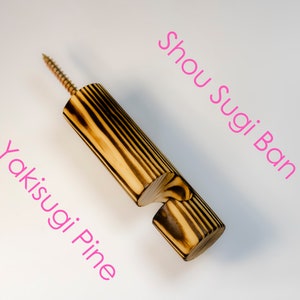 Può includere: Un gancio da parete in legno con una finitura bruciata. Il gancio è in legno di pino e ha un aspetto rustico unico. Il testo "Shou Sugi Ban" e "Yakisuji Pine" è scritto sullo sfondo bianco.