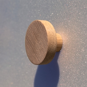 Op de afbeelding: Een ronde houten knop met een gladde, lichtbruine afwerking. De knop heeft een licht verhoogde rand en een cilindrische basis.