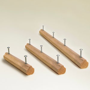 May include: Three wooden dowels with rounded ends and metal nails protruding from the top. The dowels are arranged in a staggered pattern, with the largest dowel at the back and the smallest dowel at the front.