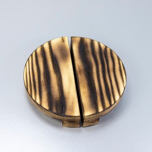 May include: A pair of round, wooden drawer pulls with a dark brown, burnt wood finish. The pulls are split in half and have a slightly raised edge.