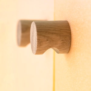 May include: Two wooden knobs with a rounded shape and a curved hook on the side. The knobs are mounted on a light brown surface.