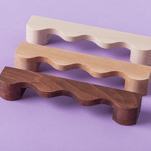 May include: Three wooden cabinet pulls with a wavy design. The pulls are in different shades of brown, from light to dark.