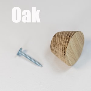 May include: A wooden knob with a natural finish and a screw. The knob is made of oak wood and has a rounded shape. The text "Oak" is visible in the image.