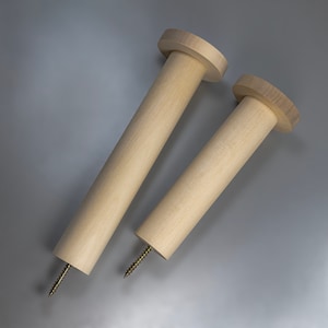 May include: Two wooden dowels with screw threads at the bottom. The dowels are unfinished and have a natural wood color. The larger dowel is about 10 inches long and the smaller dowel is about 7 inches long.