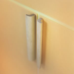 Può includere: Due maniglie per ante di armadio in legno con forma rettangolare arrotondata. Le maniglie sono montate su una parete di colore arancio chiaro.