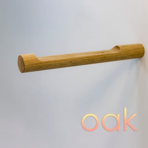 May include: A wooden towel bar made of oak with a rounded end and a cutout in the middle. The bar is mounted on a white wall with the word "oak" printed below it.