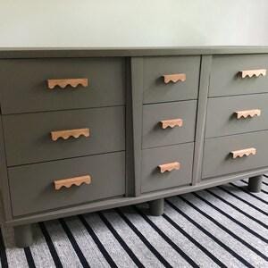 May include: A grey dresser with eight drawers and wooden knobs. The dresser has a slightly distressed finish and sits on four legs.