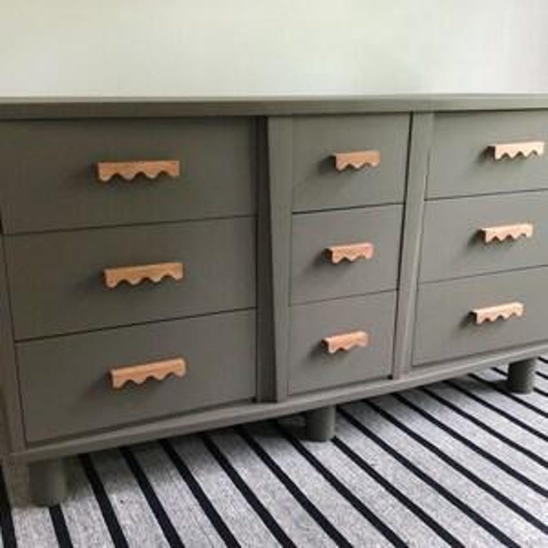 May include: A grey dresser with eight drawers and wooden knobs. The dresser has a slightly distressed finish and sits on four legs.