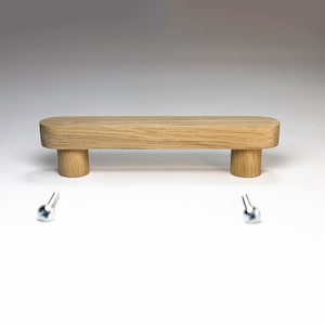 May include: A wooden drawer pull with rounded edges and two cylindrical supports. Two silver screws are included.