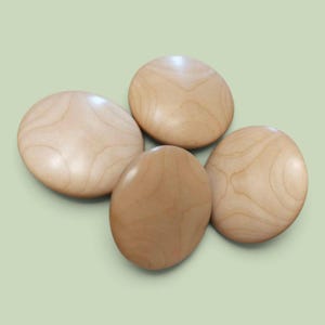 Puede incluir: Cuatro botones circulares de madera con un acabado liso y pulido. Cada botón muestra un color bronceado claro con patrones de grano de madera natural visibles que se arremolinan en la superficie. Los botones están dispuestos en grupo.