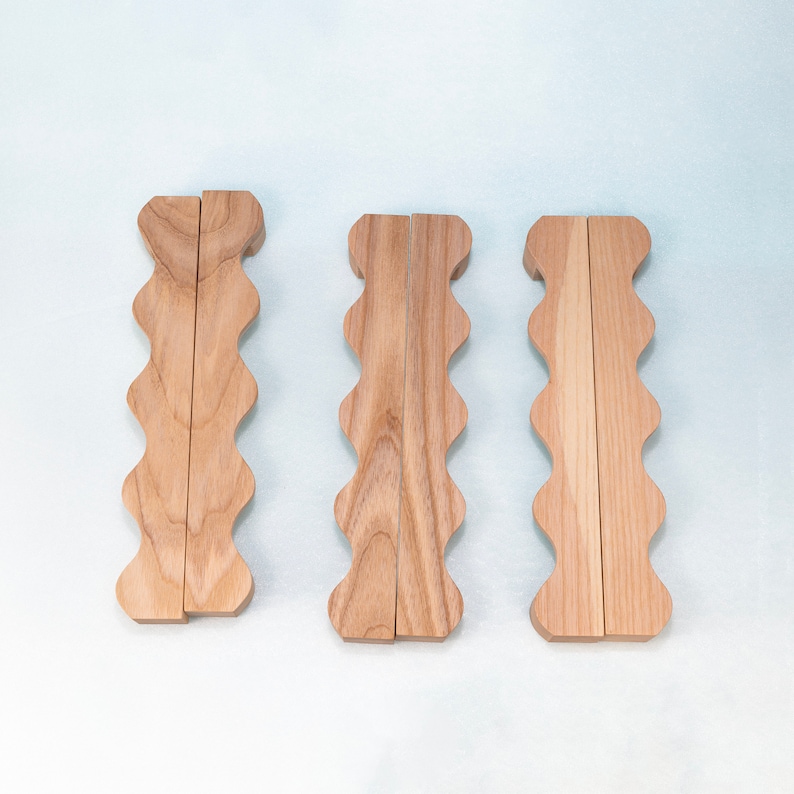 May include: Three wooden drawer pulls with a wavy edge design. The pulls are made of light brown wood and have a natural finish.