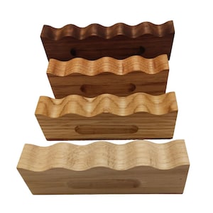 May include: Four wooden phone stands in different shades of wood. Each stand has a wavy top and a cutout for a phone.