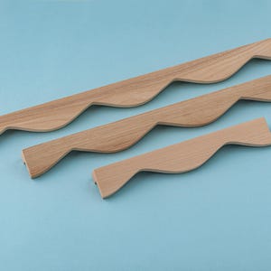 Könnte beinhalten: Drei Holzknaufgriffe mit wellenförmigem Design. Die Griffe sind in verschiedenen Größen und in einer Reihe auf einem hellblauen Hintergrund angeordnet.