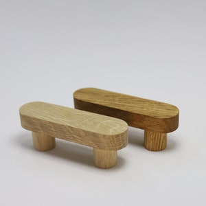 May include: Two wooden drawer pulls with a rounded rectangular shape. The pulls are made of light brown wood and have a smooth finish.