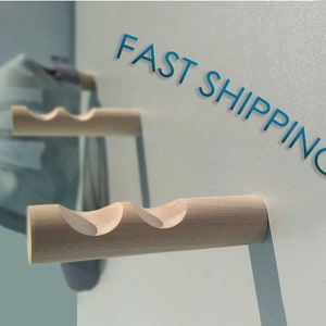 May include: Two wooden wall-mounted hooks with a wavy design. The hooks are made of natural wood and have a light brown colour. The text "FAST SHIPPING" is written in blue on a white background.