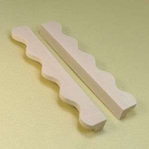 May include: Two white wooden cabinet pulls with a wavy edge design.
