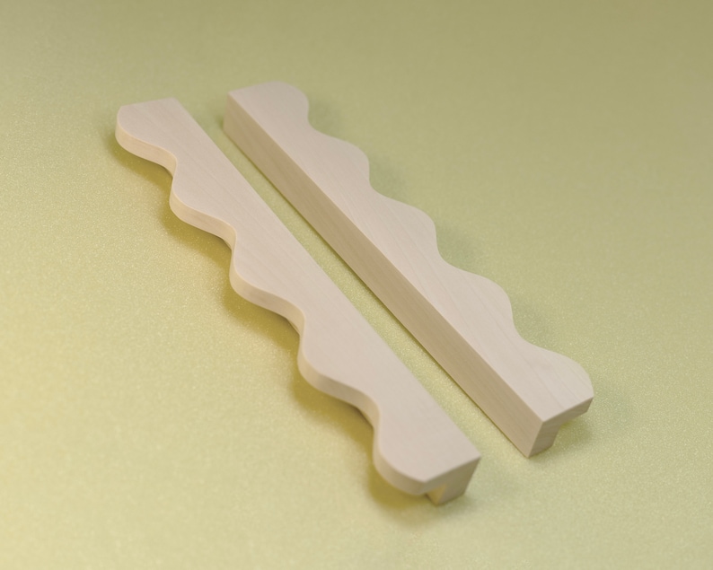 May include: Two white wooden cabinet pulls with a wavy edge design.