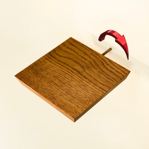 Peut inclure: Une étagère en bois brun clair avec un bord biseauté. L'étagère est fixée au mur avec une vis et une flèche rouge indique le sens de rotation.