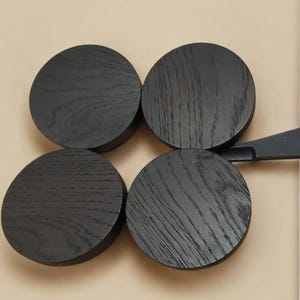 May include: Four black round wooden coasters with a wood grain pattern.