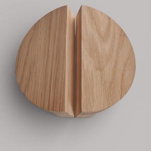 May include: A pair of semi-circular light brown oak wood cabinet handles positioned together to form a circle. The word oak is printed in dark grey text above the wooden handles. The wood grain is visible on the surface of both pieces.